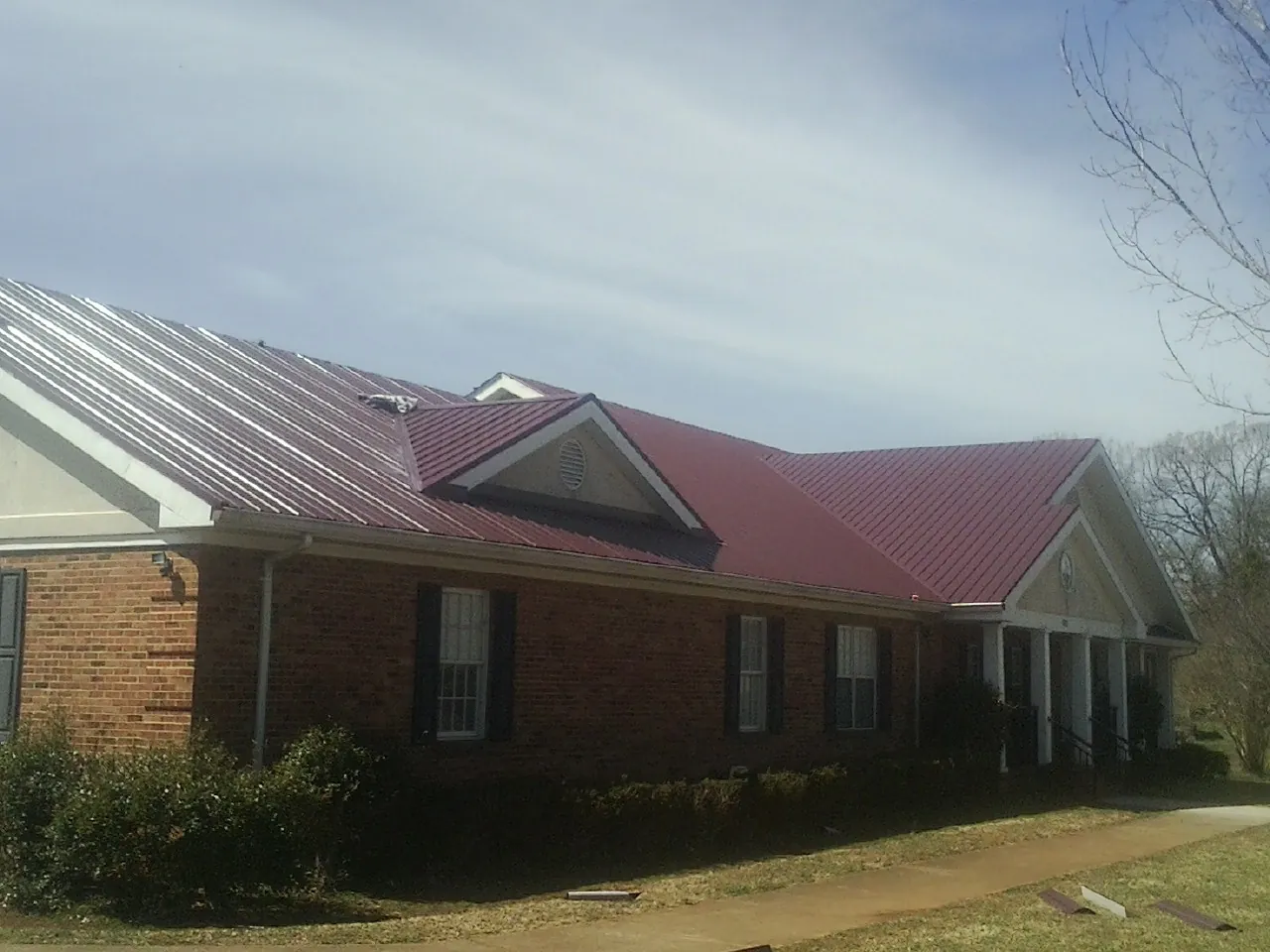 Red metal roof with gabled entries on a long brick building, from a Hail Damage Roof Repair job in Mesquite